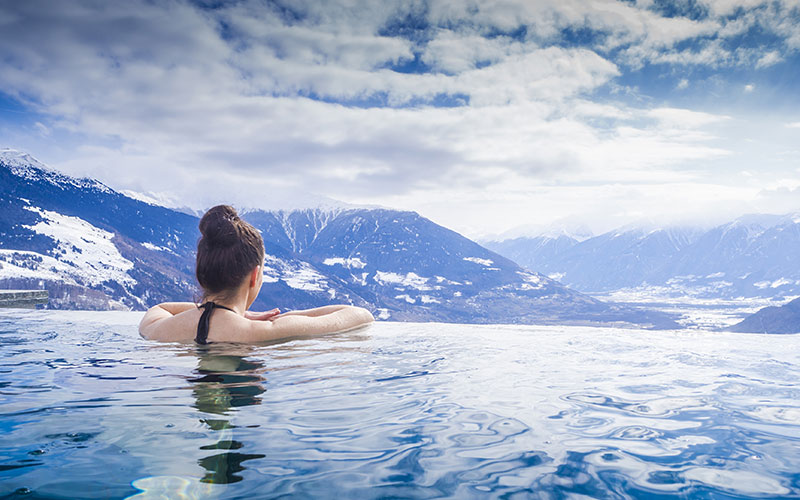 Frau im Außenswimmingpool blickt auf die Berge mit Schnee