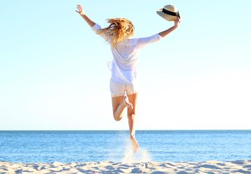 Frau springt am Strand vor dem Meer