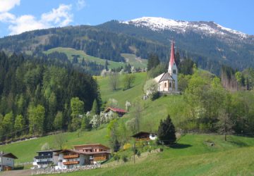 Eine Kirche in Fügen umgeben vom Wald und einer Ortschaft