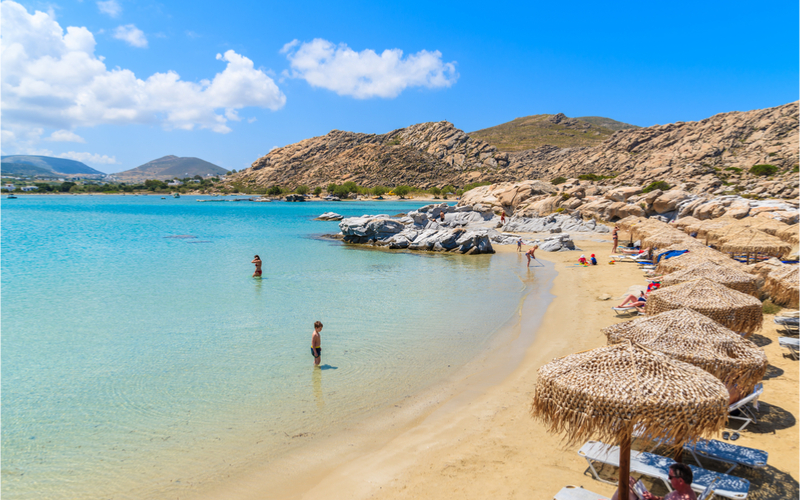 Sandstrand mit kristallklarem Meer, Felsen im Meer und Sonnenschirmen am Strand